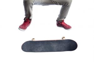 "Skateboarder wearing tan skinny jeans and red hi-top skateshoes. Framed from the waist down. Ollie kick flip, board in mid flip. Isolated on white."