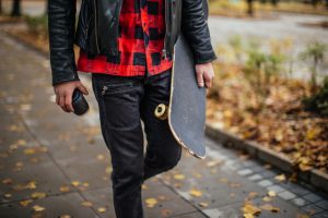 Hipster holding a coffee cup and a skateboard while walking in the park in autumn.